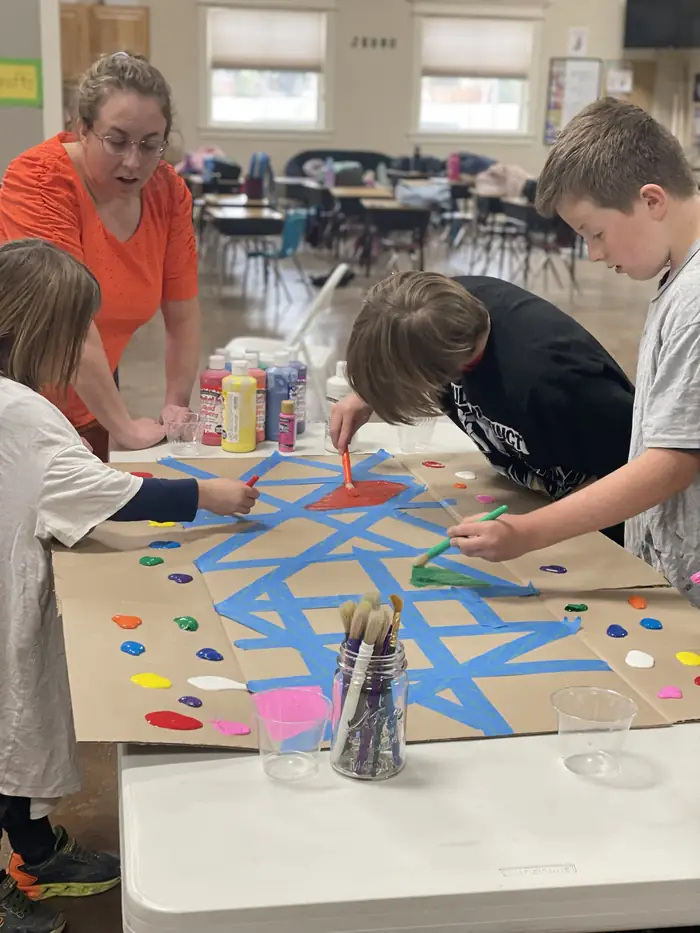 Cornerstone students painting a large taped cardboard panel together in art class