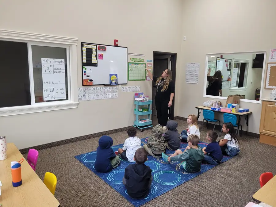 Young Cornerstone students sitting on a rug while their teacher points to the September calendar