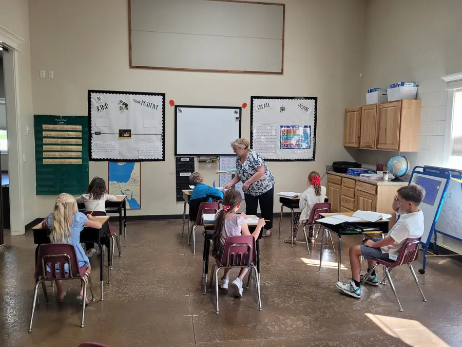 A teacher helping a student at his desk while classmates work in a Cornerstone Community Schoolhouse classroom