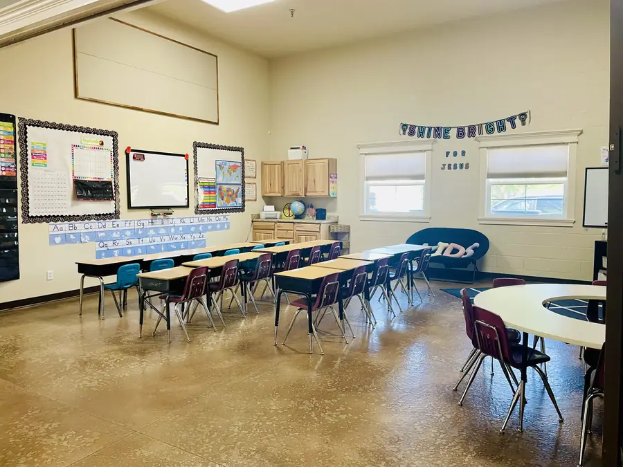 A Cornerstone Community Schoolhouse classroom with rows of desks and a Shine Brightly for Jesus banner over the windows
