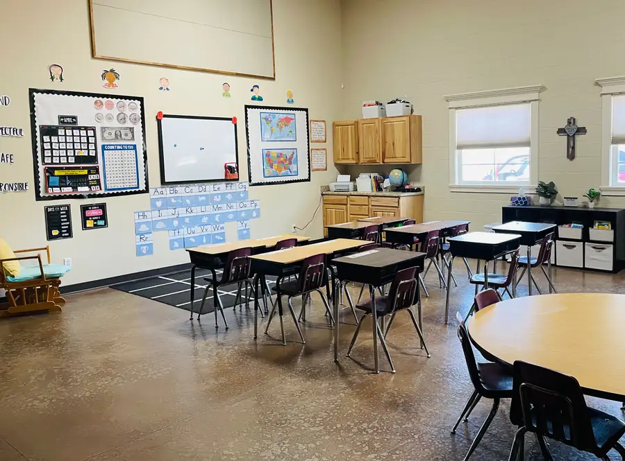 Classroom at Cornerstone Community Schoolhouse with student desks, a wall calendar, maps and a cross