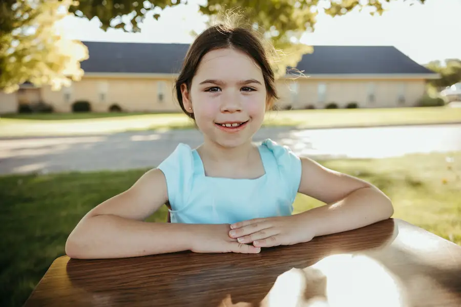 A Cornerstone Community Schoolhouse student smiling with her arms folded on a school desk outside the school