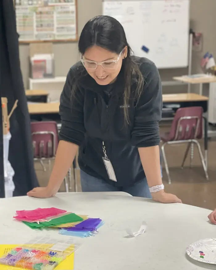 A teacher helping students make beaded bracelets to raise money for missionaries