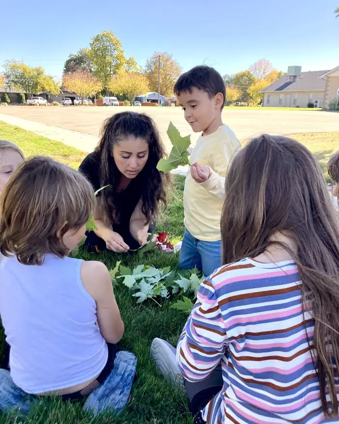 A teacher and students studying leaves on the grass during an outdoor lesson in Caldwell, Idaho