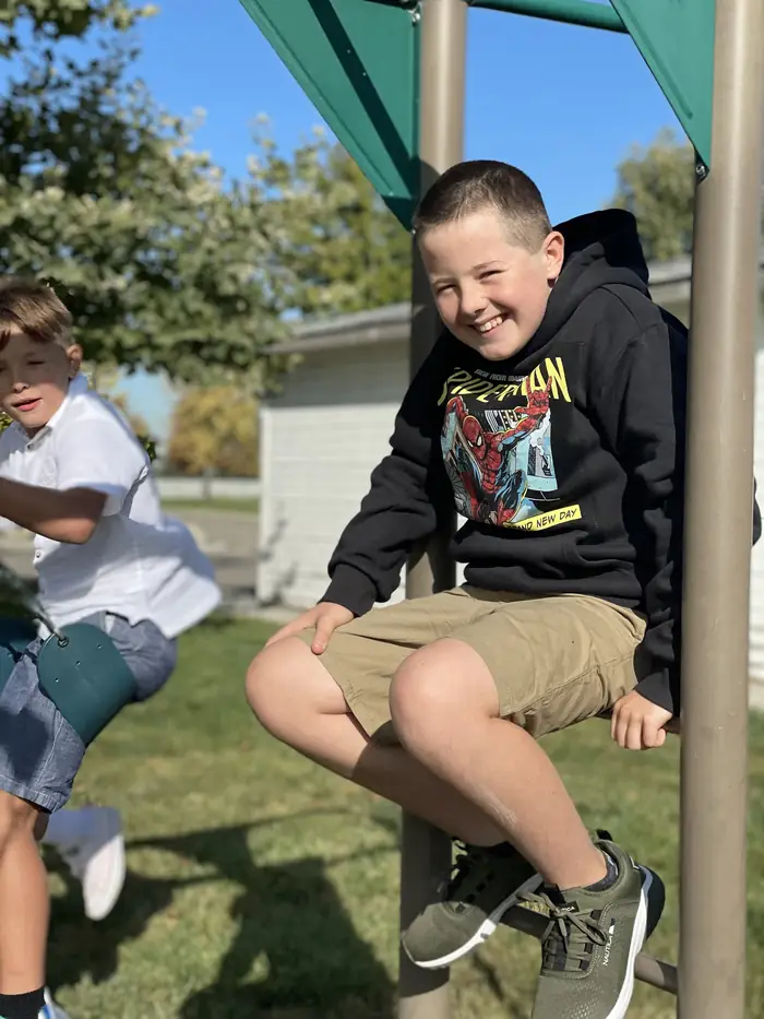 A Cornerstone student smiling while sitting on the playground climbing frame