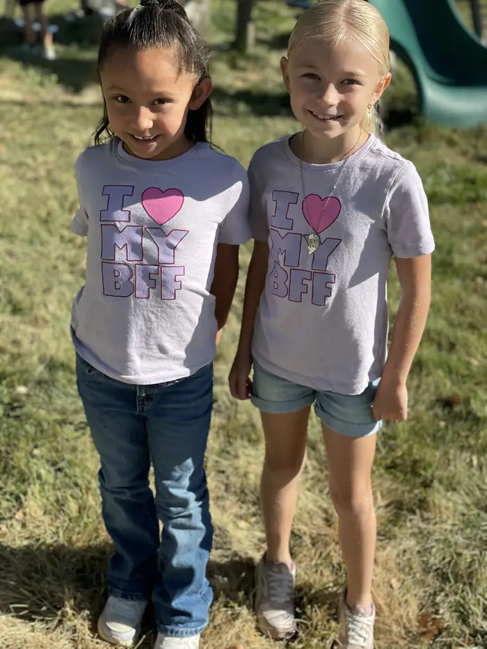 Two Cornerstone students in matching shirts smiling on the playground lawn